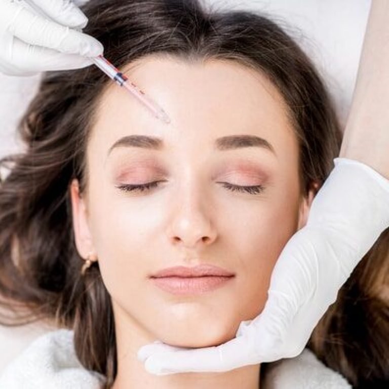Woman receiving a botox injection in the eye zone lying in bathrobe on the medical couch